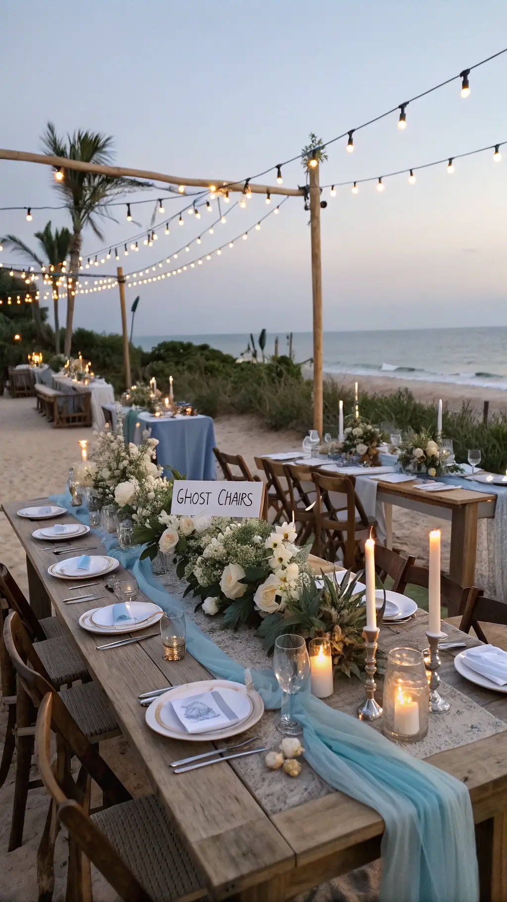 Oceanfront dining setup with farm tables, blue runners, brass candlesticks, orchids, sea glass, and copper vessels at sunset.