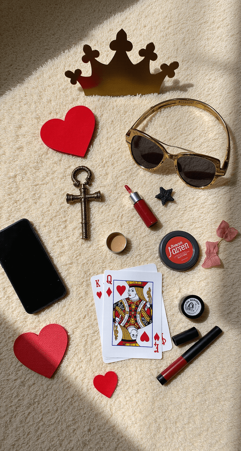 A budget-friendly flat lay on a plush cream carpet features DIY Queen of Hearts accessories, including a handcrafted paper crown, a painted dollar store scepter, playing card details, and drugstore red and black makeup essentials, all illuminated by mid-morning sunlight. An iPhone and craft supplies hint at the accessible creation process, captured in an overhead shot that emphasizes the creative arrangement.