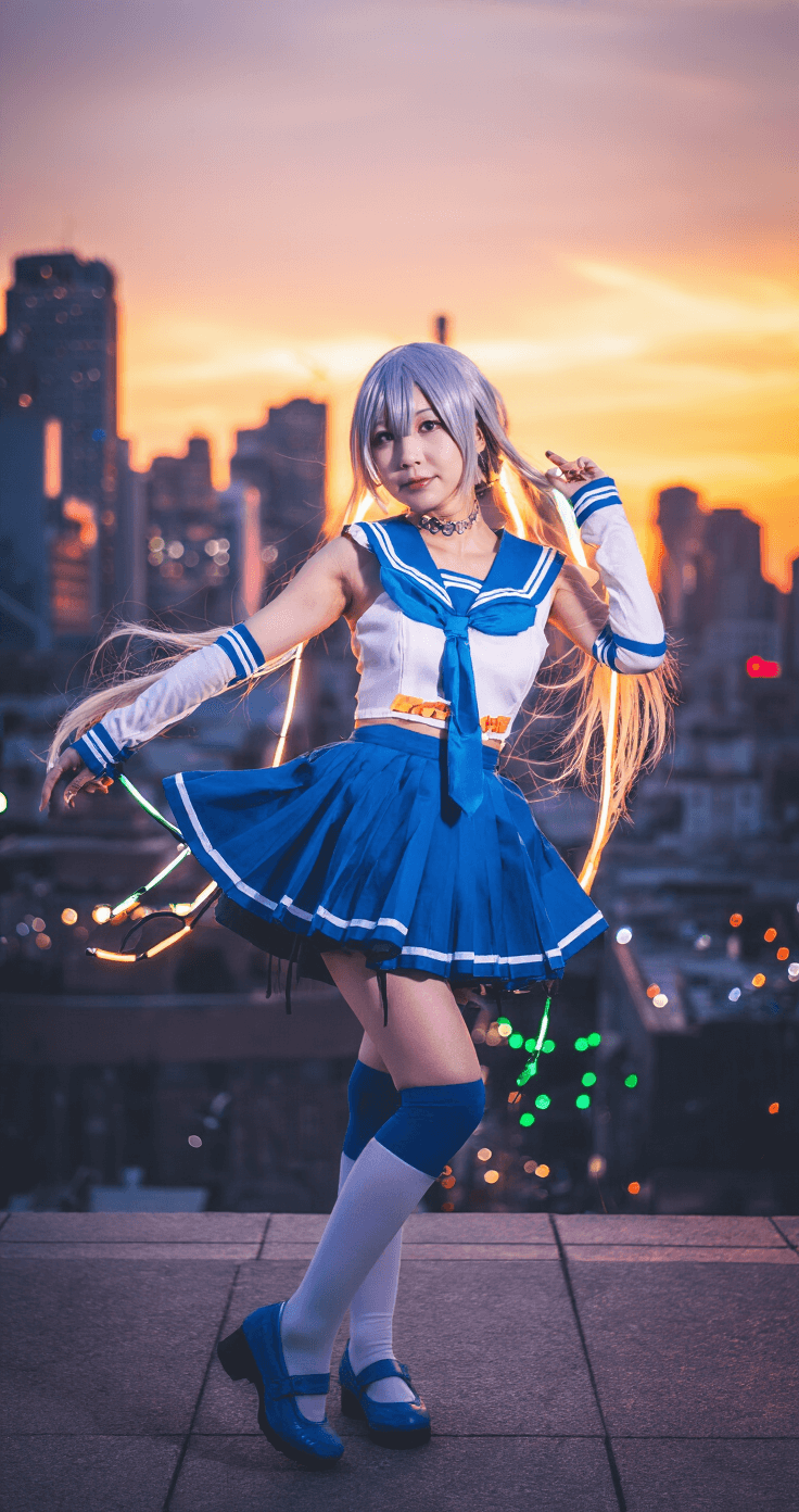 A cosplayer poses dynamically on an urban rooftop at sunset, showcasing a vibrant costume with twin-tails and a pleated skirt. The city skyline glows in the background, enhanced by LED strips and the warm golden hour light, while cool tones of the wig contrast against the bokeh lights of the city.