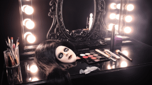 A professional vanity workspace set up for horror makeup, featuring dramatic supplies like a long black wig, white contact lenses, SFX prosthetics, and false eyelashes, illuminated by warm LED lights and surrounded by a gothic mirror and silver makeup tools.
