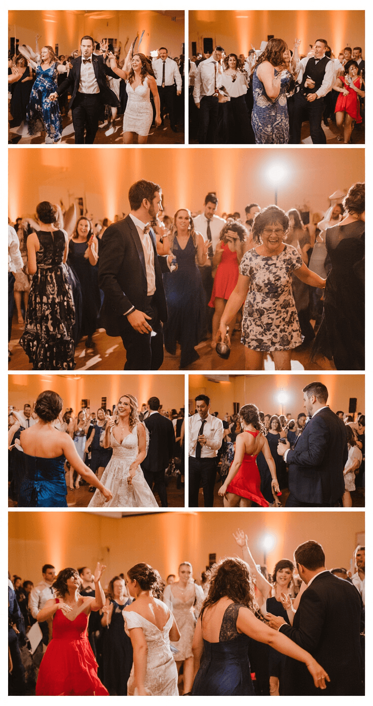A lively wedding reception dance floor filled with guests in semi-formal attire, featuring women in jewel-toned dresses and men in tailored suits, illuminated by warm amber uplighting, with a live band in the background and dynamic motion captured through soft blur and lens flare.