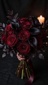 Dark romantic wedding bouquet with burgundy roses and black calla lilies illuminated by candlelight