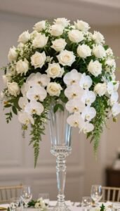 Luxury wedding flower arrangement with white roses, orchids and greenery in a tall crystal vase