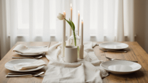 Cinematic overhead shot of a minimalist wedding reception tablescape featuring a cream linen runner, a single white tulip in a glass vase, simple white dinnerware, flickering pillar candles, and soft natural daylight filtering through sheer curtains, evoking calm elegance and sophistication.