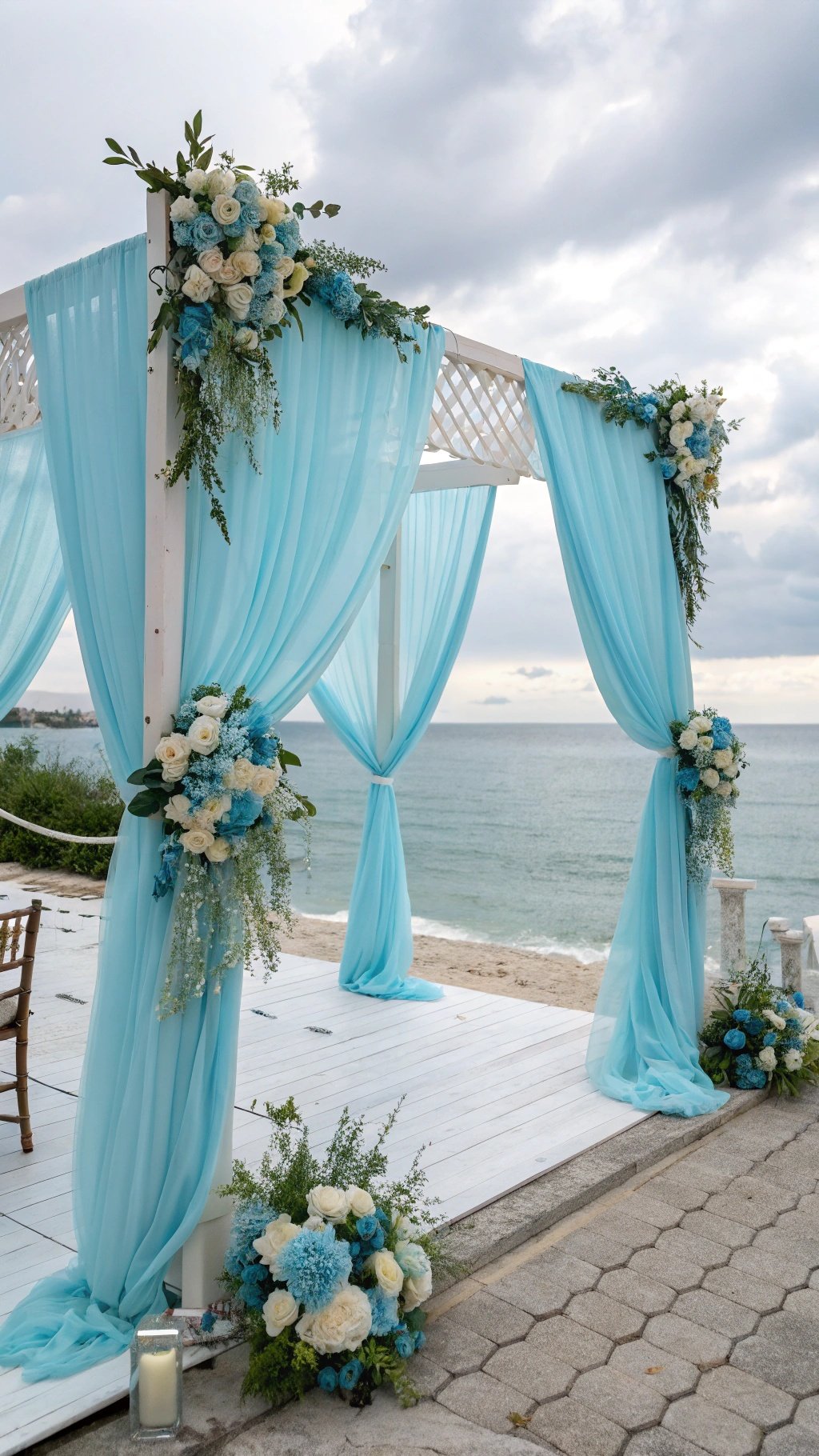 A serene baby blue wedding ceremony backdrop with draped fabric and floral arrangements by the beach.