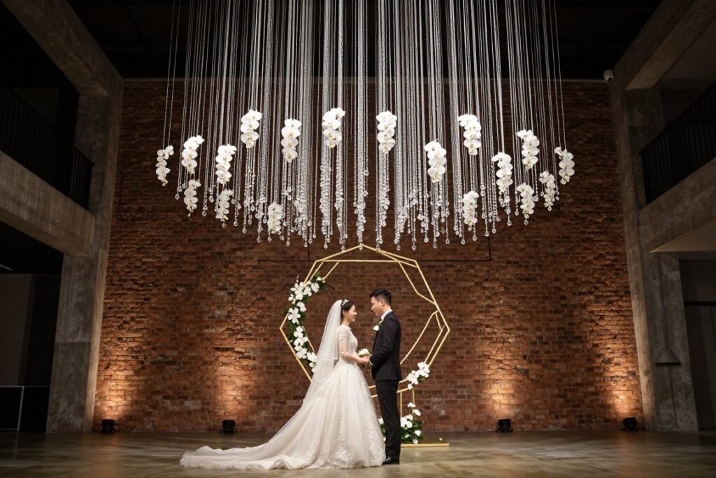 A suspended geometric gold halo wedding backdrop with white orchids and hanging crystal elements in a modern loft venue